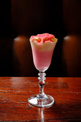 An exquisite pink cocktail topped with vibrant foam stands elegantly on a polished wooden surface