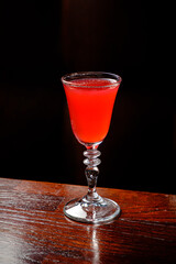 A striking red cocktail sits on a polished wooden surface, exuding elegance and allure