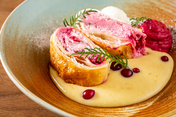 A beautiful dessert plate with a fruity pastry roll, creamy sauce, and garnishes
