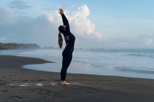 Woman practicing yoga at beach against clear sky during sunset
