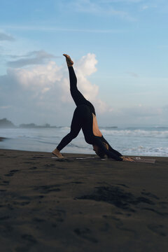 Woman practicing yoga at beach against clear sky during sunset