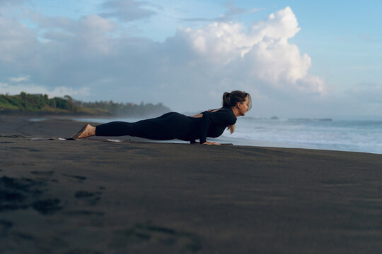 Woman practicing yoga at beach against clear sky during sunset