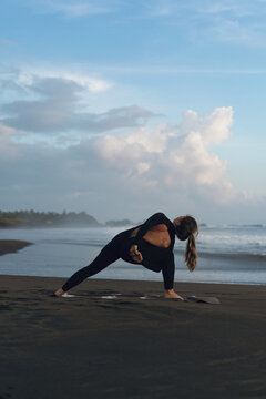 Woman practicing yoga at beach against clear sky during sunset