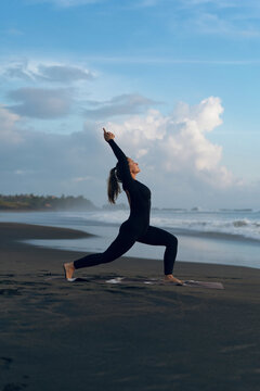 Woman practicing yoga at beach against clear sky during sunset