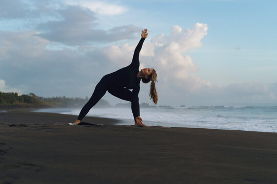 Woman practicing yoga at beach against clear sky during sunset