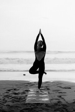 Woman practicing yoga at beach against clear sky during sunset