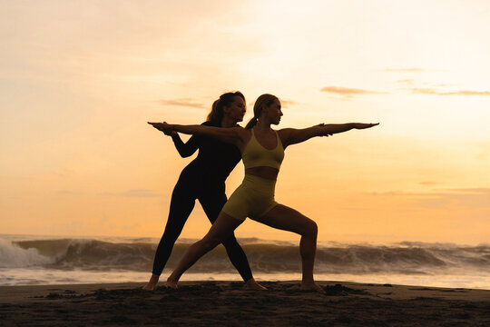 Instructor assisting woman in yoga posture in the beach