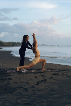 Instructor assisting woman in yoga posture in the beach