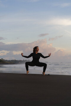 Woman practicing yoga at beach against clear sky during sunset