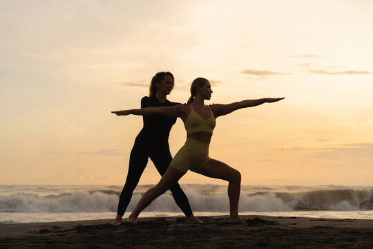 Instructor assisting woman in yoga posture in the beach