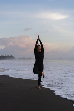 Woman practicing yoga at beach against clear sky during sunset