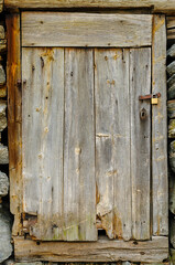 A weathered wooden door stands firmly against a stone wall, showcasing its rustic charm and natural wear, with a padlock securing it.