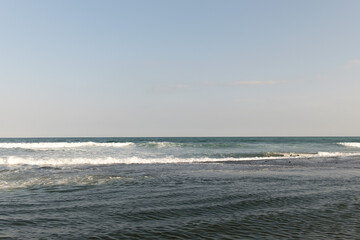 春のかすみがかった青空と白く打ち寄せる波と波紋が風に揺れる水面