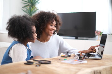 Naklejka premium African loving mother and daughter team up for fun robotics project at home, exploring hands-on STEM activities that inspire creativity, and early engineering skills, fostering problem-solving skills