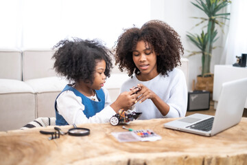 African loving mother and daughter team up for a fun robotics project at home, exploring hands-on...