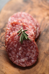 Sliced salame milano sausage on olive wood board with rosemary