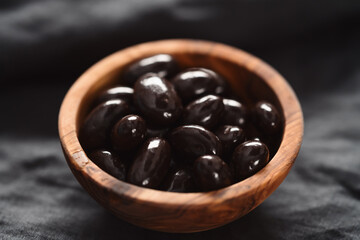 Dark chocolate dragee in olive wood bowl on linen background
