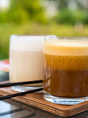 Two glasses of coffee sit on a wooden tray, one of which is filled with a frothy