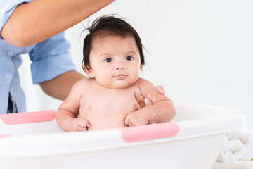 Asian mother bathing her 3 months newborn baby in bathtub at home, mom cleaning her cute little daughter with liquid soap and sponge. Baby have fun bathing with mom