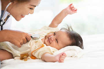 Smiling Asian female pediatrician listens to newborn's heartbeat with a stethoscope. Doctor gently...
