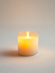 A glowing wax light in a glass holder casting a warm light on a neutral background scene