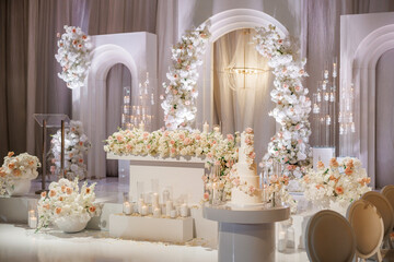 Luxurious wedding decoration with beautiful flower arrangements in white colors indoors. A wedding banquet with many flowers, arches and burning candles in glass candlesticks for a romantic atmosphere