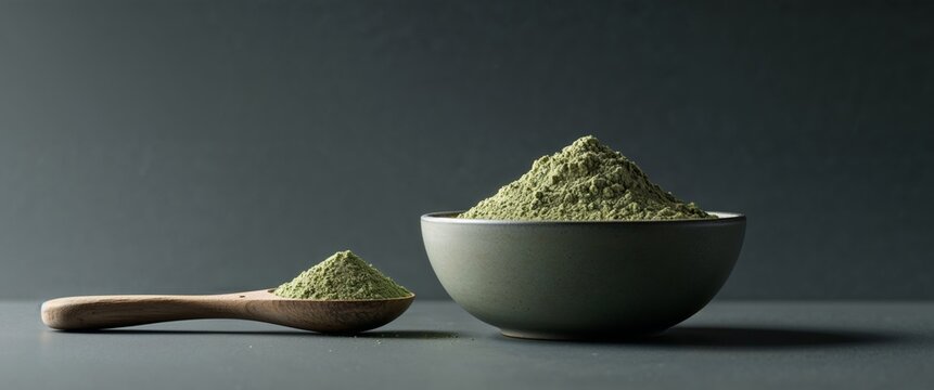 a bowl filled low saturated green Hemp powder next to a wooden spoon on top of a dark background.