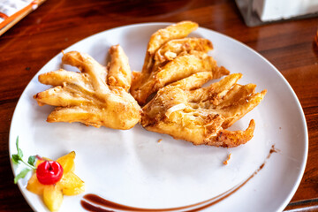 Crispy fried banana pieces on a white plate, garnished with starfruit and cherry. Warm wood table background. Overhead shot with natural light highlighting texture.