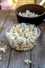 Bowl of popcorn on rustic wood table, pot in background. Casual snack, simple treat. Natural light, some kernels scattered.