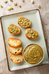 Healthy pistachio butter and toasted bread close-up on plate on table. Vertical top view from above
