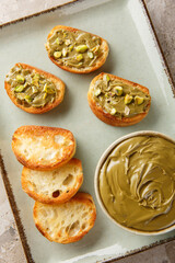 Pistachio butter in bowl with toast on plate raw pistachios closeup on the table. Vertical top view...