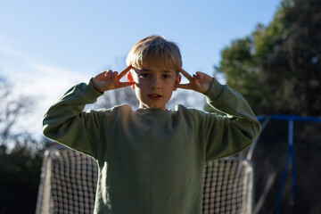 Naklejka premium Young boy making peace sign with fingers on head in garden
