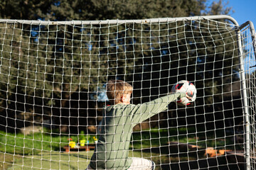 Young goalkeeper making a save during soccer training in garden