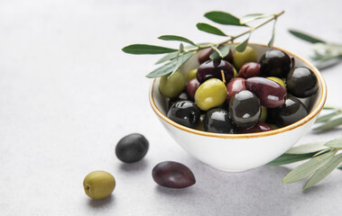 Fresh olives with olive branch in white bowl on marble table