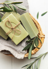 Natural olive soap bars with olive branches in wicker basket on white tiles