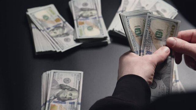 A man counts stacks of money, many dollars at the table and checks them for authenticity