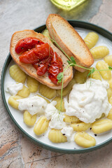Potato gnocchi with stracciatella cheese and roasted tomato bruschettas, vertical shot, middle close-up, selective focus