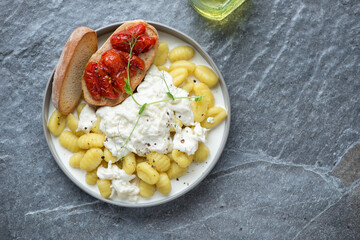 Plate of italian gnocchi served with stracciatella cheese, above view on a dark-grey granite background, horizontal shot with space