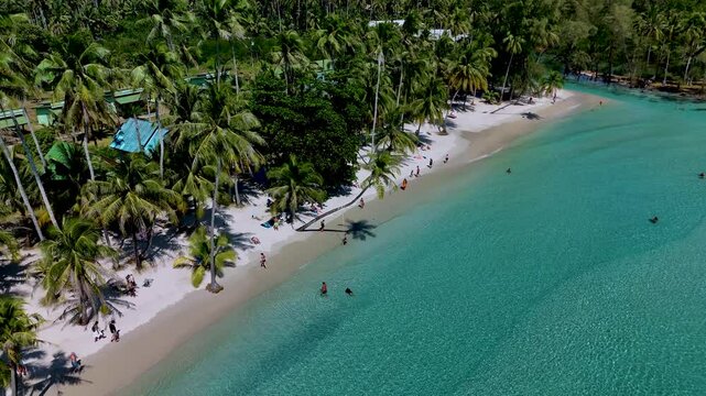 Immerse yourself in the beauty of Koh Kood Thailands sandy shores with palm trees swaying gently. Sunbathers enjoy the sun, while others wade in the turquoise waters.