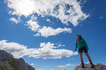 Girl standing on a boulder looking at the sky during a hike in the Dolomites, Mount Latemar, Trentino, Italy. Traveling photography and outdoor sport activity concept