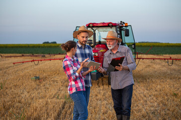 Group of farmers talking in front of tractor in field in summer