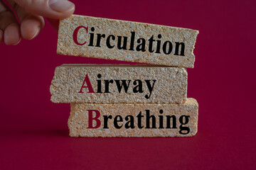 Concept words CAB-Circulation, Airway, Breathing on brick blocks. Beautiful red background. Doctors hand. Symbol for basic life support.