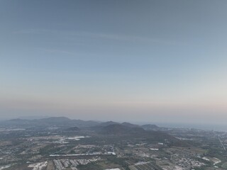 Aerial panoramic view of a vast rural landscape with distant mountain ranges under a clear blue sky, featuring a diagonal airplane contrail stretching across the horizon