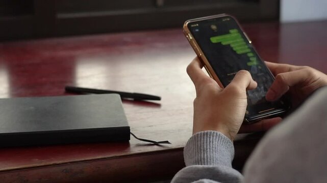 man's hand is typing on the cellphone screen to send a message near the work desk