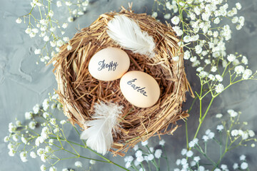 Two chicken eggs with the inscription Happy Easter in a nest of dry grass with feathers and...