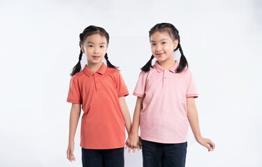 Obraz premium Two young girls with braided hair hold hands, smiling in matching shirts and dark pants on a white background.