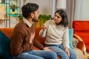 Upset young Arabian couple arguing fighting while sitting on sofa in living room at home. Divorce...