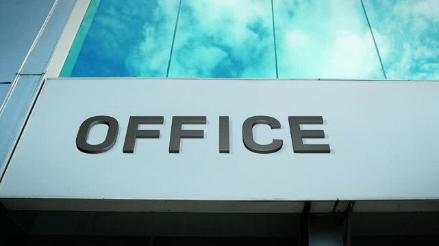 Office sign on a modern building with a reflection of the sky on glass windows, symbolizing work, business, and professional environment