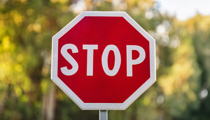 Classic red stop sign, octagon with bold white lettering, set against blurred bokeh background.