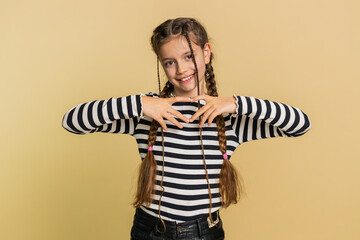 Fototapeta premium Girl in love. Smiling attractive young preteen child kid makes heart gesture demonstrates love sign expresses good positive feelings and sympathy. Teenager children isolated on beige background
